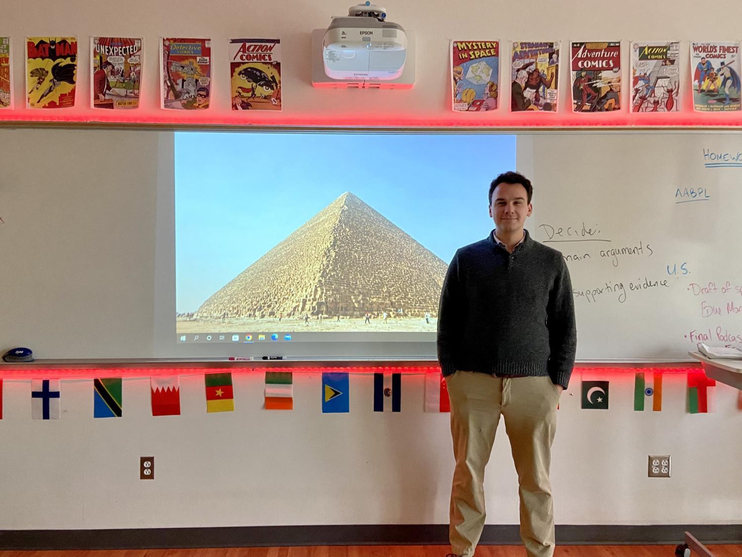 Mr. Ames poses in front of his wallpaper, a pyramid, in his classroom.