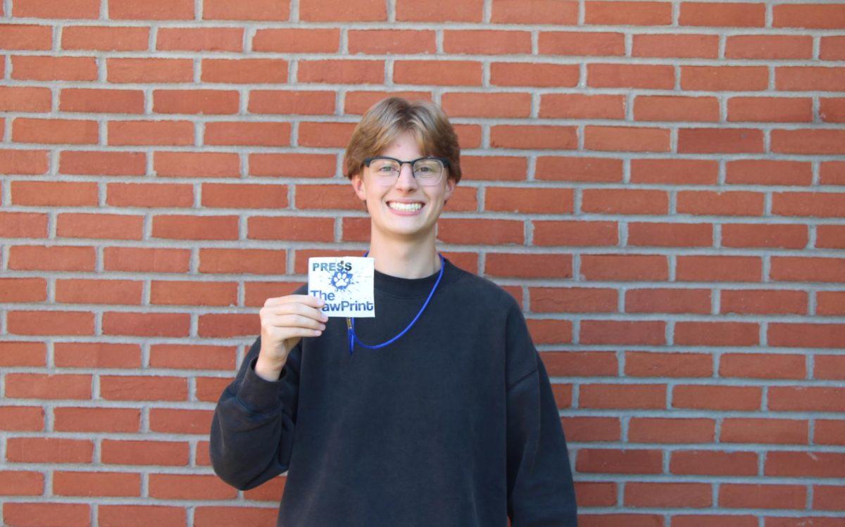Picture of Sean Davis standing in front of brick wall holding a Morgan PawPrint Pass.