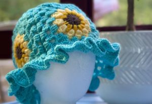 A crocheted light blue sunhat with sunflowers on it.