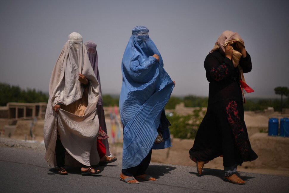 Afghan women walk along the side of the road.