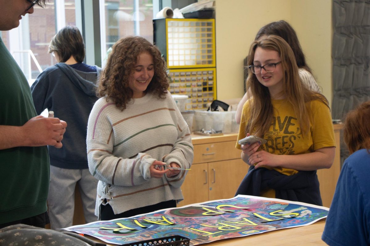 A group of students standing over a poster, talking and smiling while they work on it.